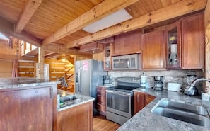 A wooden cabin interior with a kitchen featuring a refrigerator, microwave, stove, and sink. - Spacious Luxury Log Cabin with Game Room & Panoramic Mountain Views near Pigeon Forge, Tennessee (Sevierville)