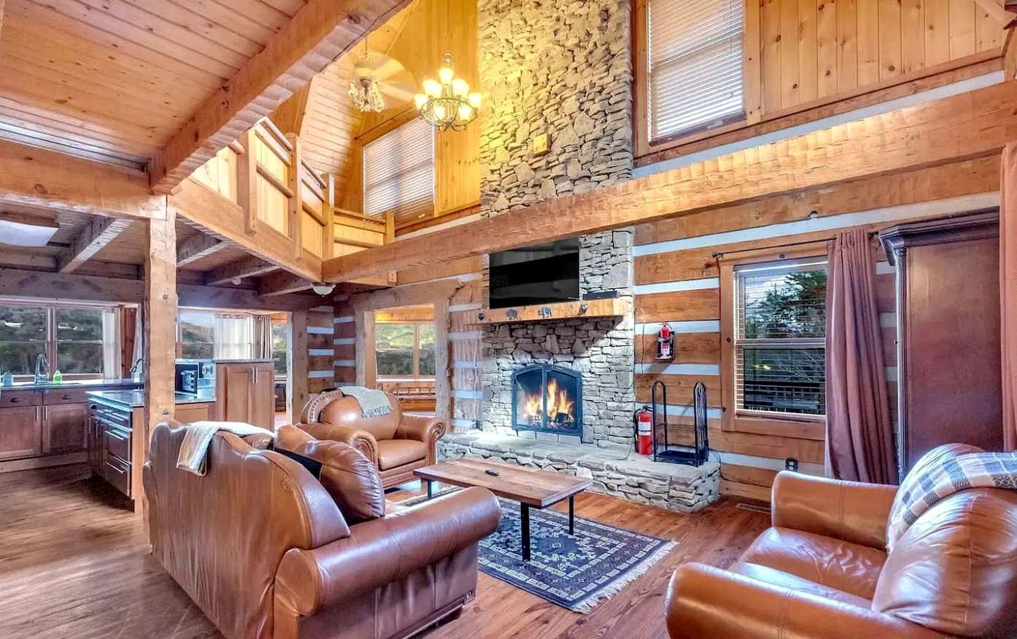 A log cabin interior with a stone fireplace, leather furniture, and wooden beams.