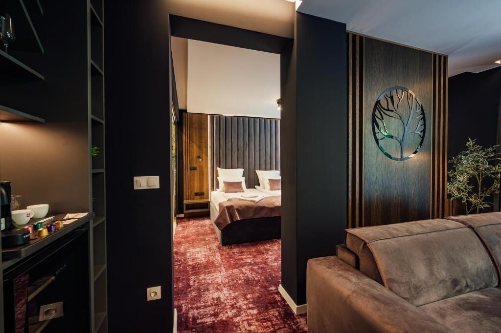 Moderni hotellihuone, jossa on sänky, punainen matto, puukoristeinen seinä ja seinään kiinnitetty valaisin.