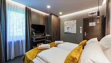 A hotel room with a bed, a desk with a television, a painting on the wall, and a door with a lock.