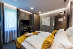 Una habitación de hotel con una cama, un escritorio con televisor, un cuadro en la pared y una puerta con cerradura.