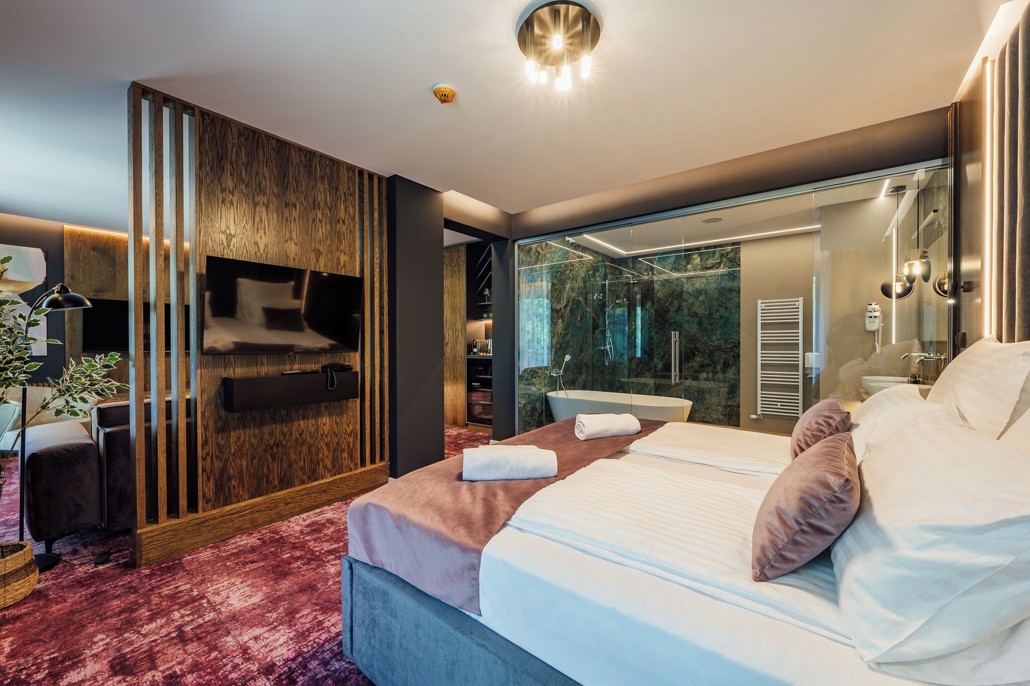 A modern hotel room with a large bed, a TV, a glass shower enclosure, and a view of the bathroom.