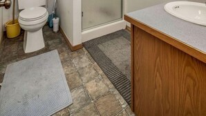 A bathroom with a toilet, sink, shower, and a window with a curtain.