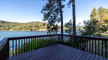A wooden deck with a railing overlooking a lake, surrounded by trees.