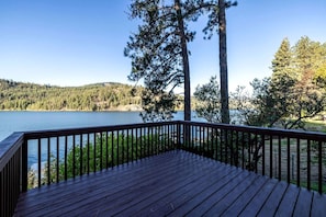 A wooden deck with a railing overlooking a lake, surrounded by trees.