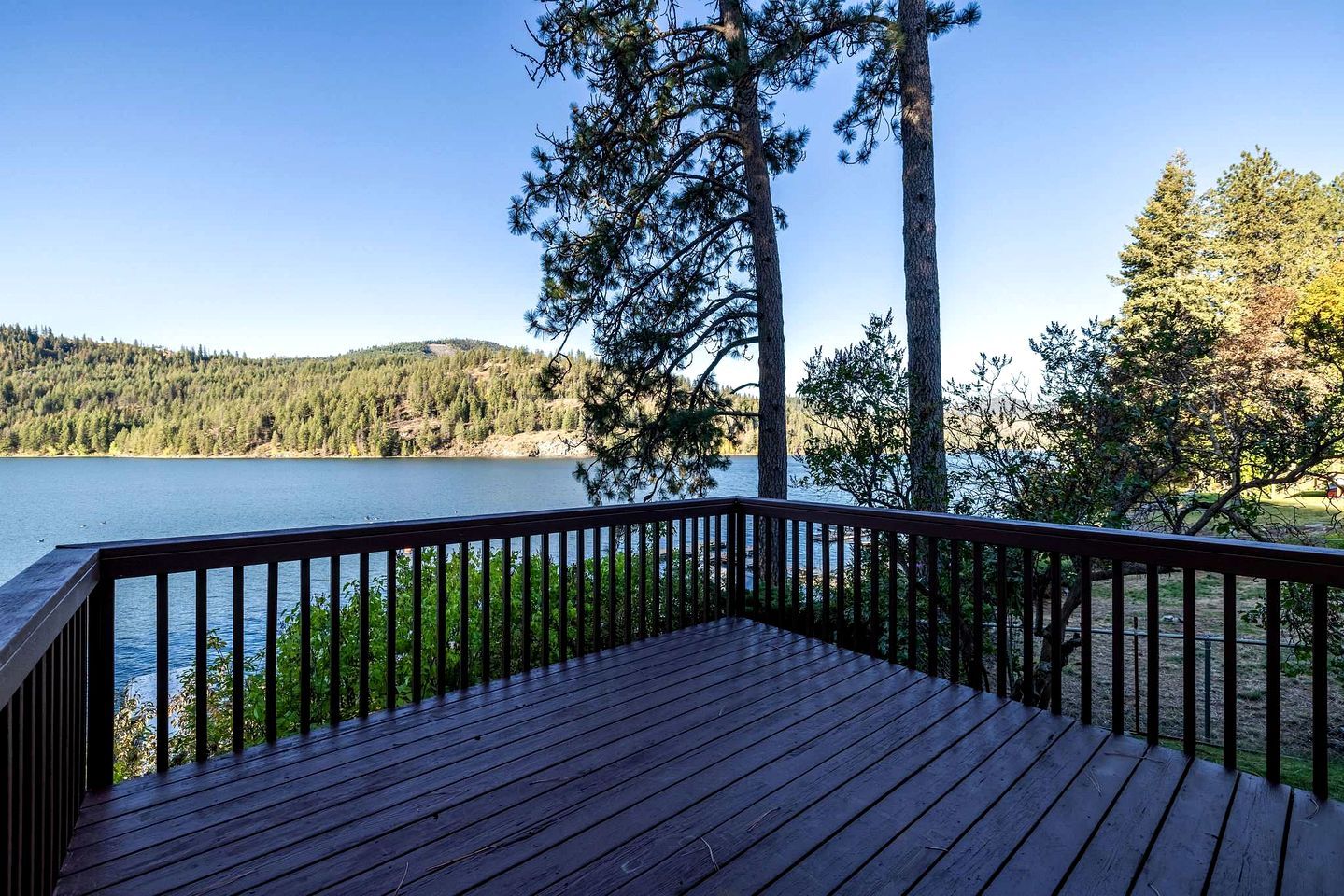 A wooden deck with a railing overlooking a lake, surrounded by trees.