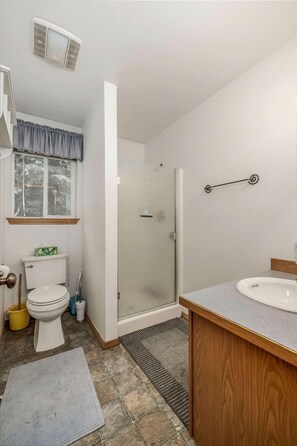 A bathroom with a toilet, sink, shower, and a window with a curtain.