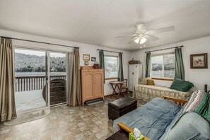 A room with a bed, a desk, a chair, a cabinet, and a view of a snowy landscape through large windows.