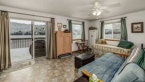 A room with a bed, a desk, a chair, a cabinet, and a view of a snowy landscape through large windows.