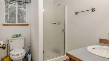 A bathroom with a toilet, sink, shower, and a window with a curtain.