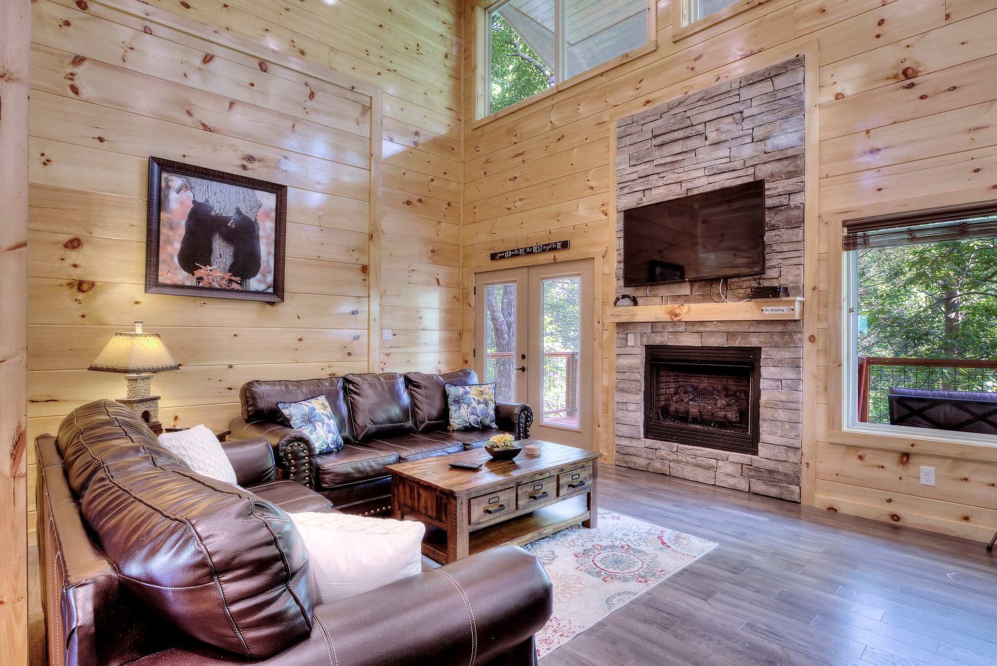 A log cabin interior with a leather sofa, fireplace, and large windows.