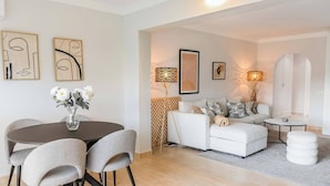 Een moderne woonkamer met een ronde eettafel, grijze stoelen, een witte bank en een tapijt met een patroon.