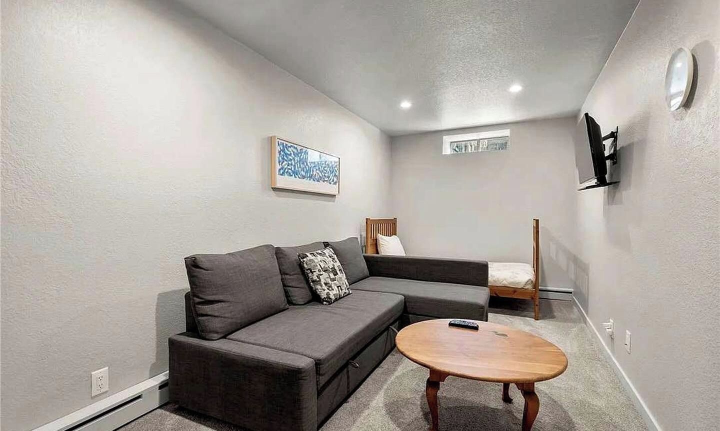 Un salon moderne avec un canapé, une petite table ronde, un téléviseur fixé au mur et une fenêtre donnant sur un beau paysage.