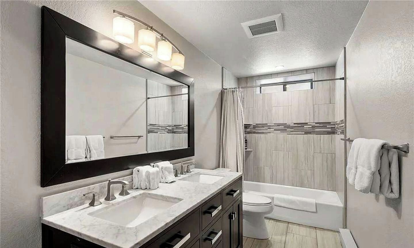A modern bathroom with a large mirror, two sinks, a toilet, and a shower area.