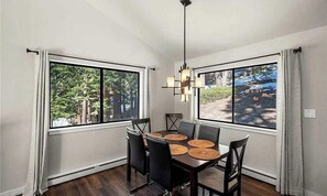 A dining area with a table set for four, large windows, and a hanging light fixture.