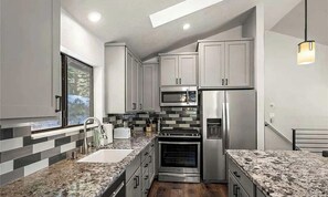A modern kitchen with stainless steel appliances, a granite countertop, and a view of the outdoors.