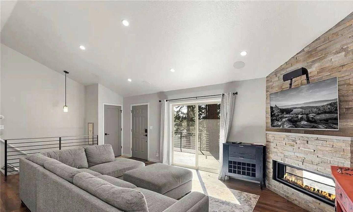 A modern living room with a fireplace, a large sofa, and a view through the glass door.
