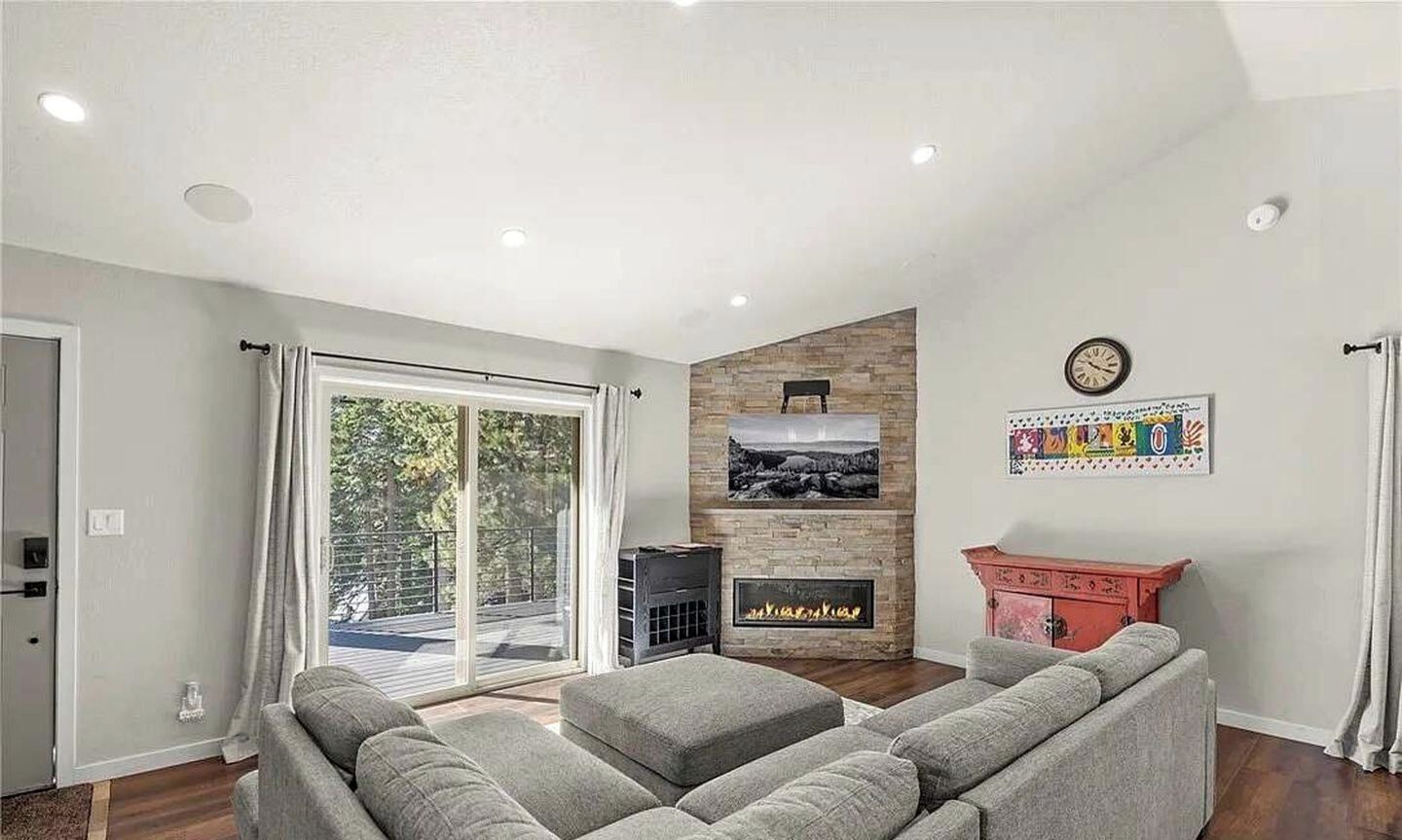 A modern living room with a fireplace, a sofa set, and a large window offering a view of the outdoors.