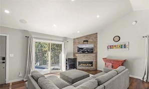 A modern living room with a fireplace, a sofa set, and a large window offering a view of the outdoors.