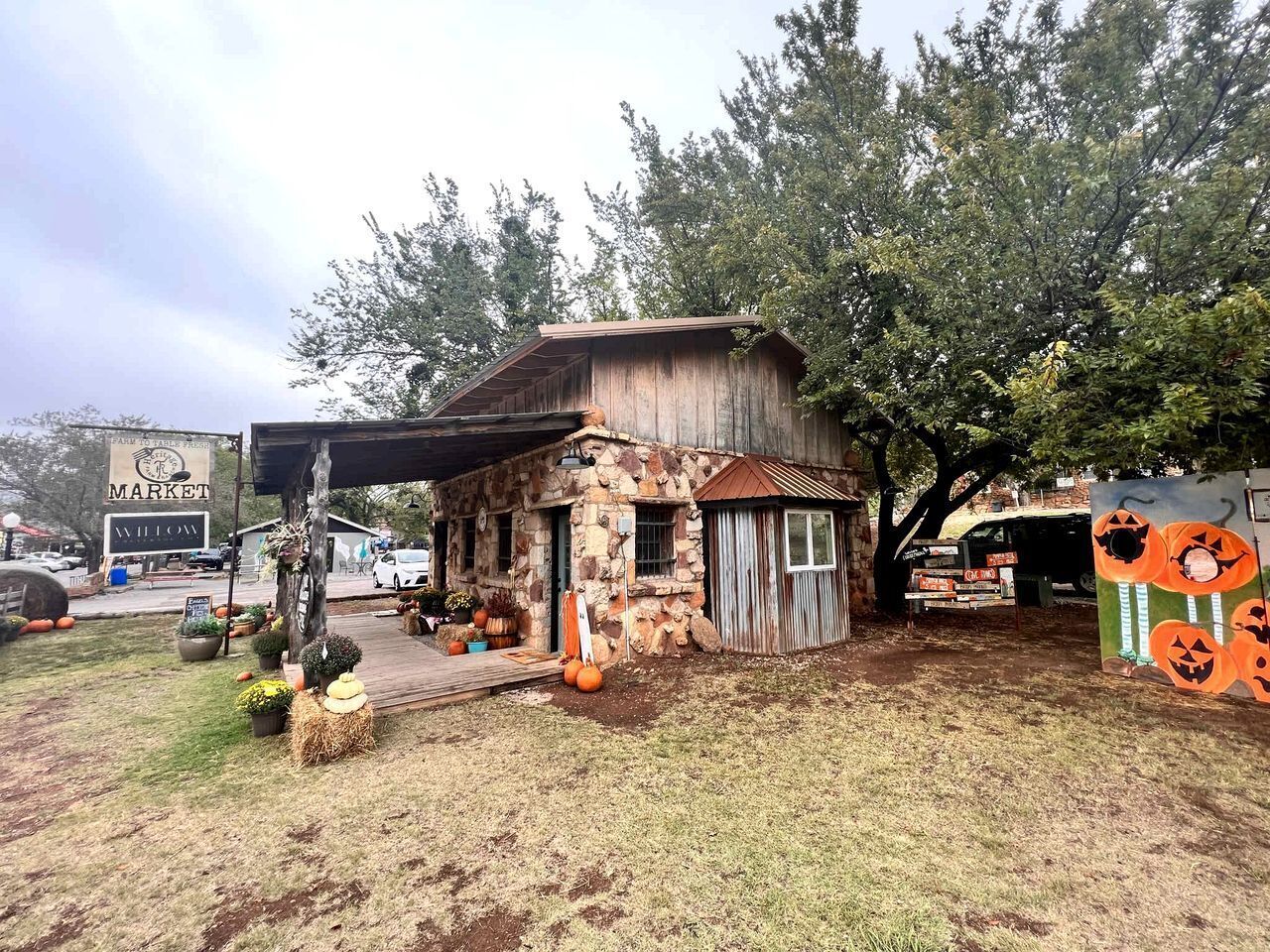 Un edificio rústico de piedra con techo de metal, rodeado de árboles y una decoración con calabaza.