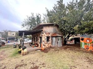 Un bâtiment rustique en pierre, surmonté d’un toit en métal, entouré d’arbres et agrémenté d’une décoration sur le thème de la citrouille.