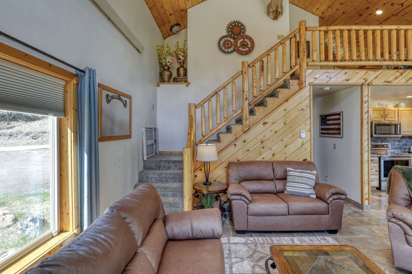A spacious living room with a wooden staircase, leather sofas, and a view of the outside.