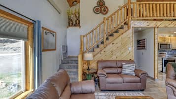 A spacious living room with a wooden staircase, leather sofas, and a view of the outside.