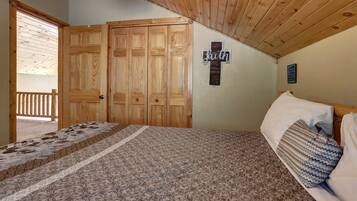 Un dormitorio con una cama, techo de madera, una cruz en la pared y una puerta que da a un balcón.