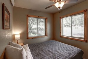 A bedroom with a bed, two windows with blinds, a ceiling fan, and a lamp. - Lush Creekside Vacation Rental Haven near Mount Rushmore in South Dakota (Keystone)