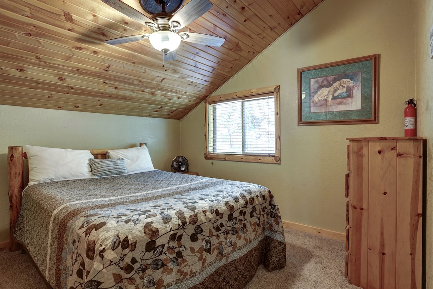 A bedroom with a bed, a ceiling fan, a window, and a painting on the wall.