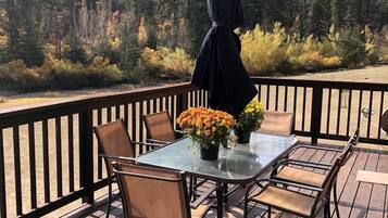 Una terraza de madera con una mesa y sillas de vidrio, rodeada por una barandilla negra.