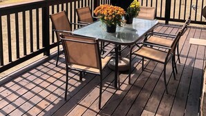 Een houten terras met een glazen tafel en stoelen, omgeven door een zwarte reling.
