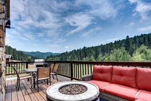 A deck with a fire pit, outdoor furniture, and a scenic forest view. - Lush Creekside Vacation Rental Haven near Mount Rushmore in South Dakota (Keystone)