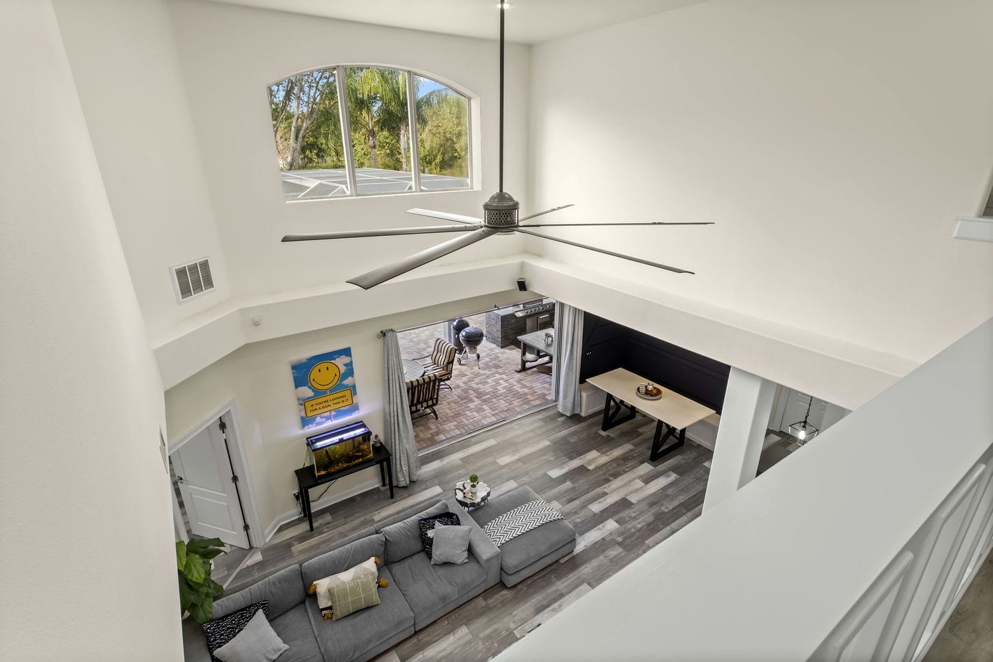 A spacious living area with a high ceiling fan, a dining table, and a large window overlooking a patio.