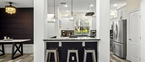 A modern kitchen with a central island, bar stools, stainless steel appliances, and pendant lighting.