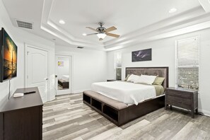 Quarto com cama, mesas de cabeceira, ventilador de teto e televisão.
