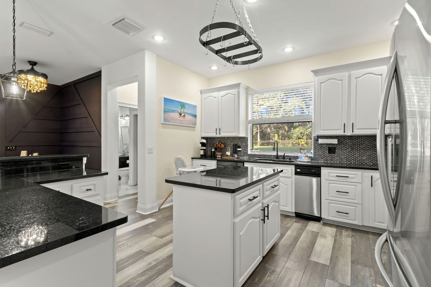 A modern kitchen with white cabinetry, a black countertop, and a stainless steel refrigerator.