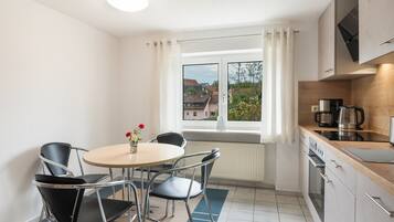 Eine kleine Küche mit Essbereich, einem Fenster mit Vorhängen und Blick auf Häuser.