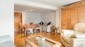 Una sala de estar con sofá, una mesa de centro de vidrio, una zona de comedor con mesa y sillas, y un armario de madera.