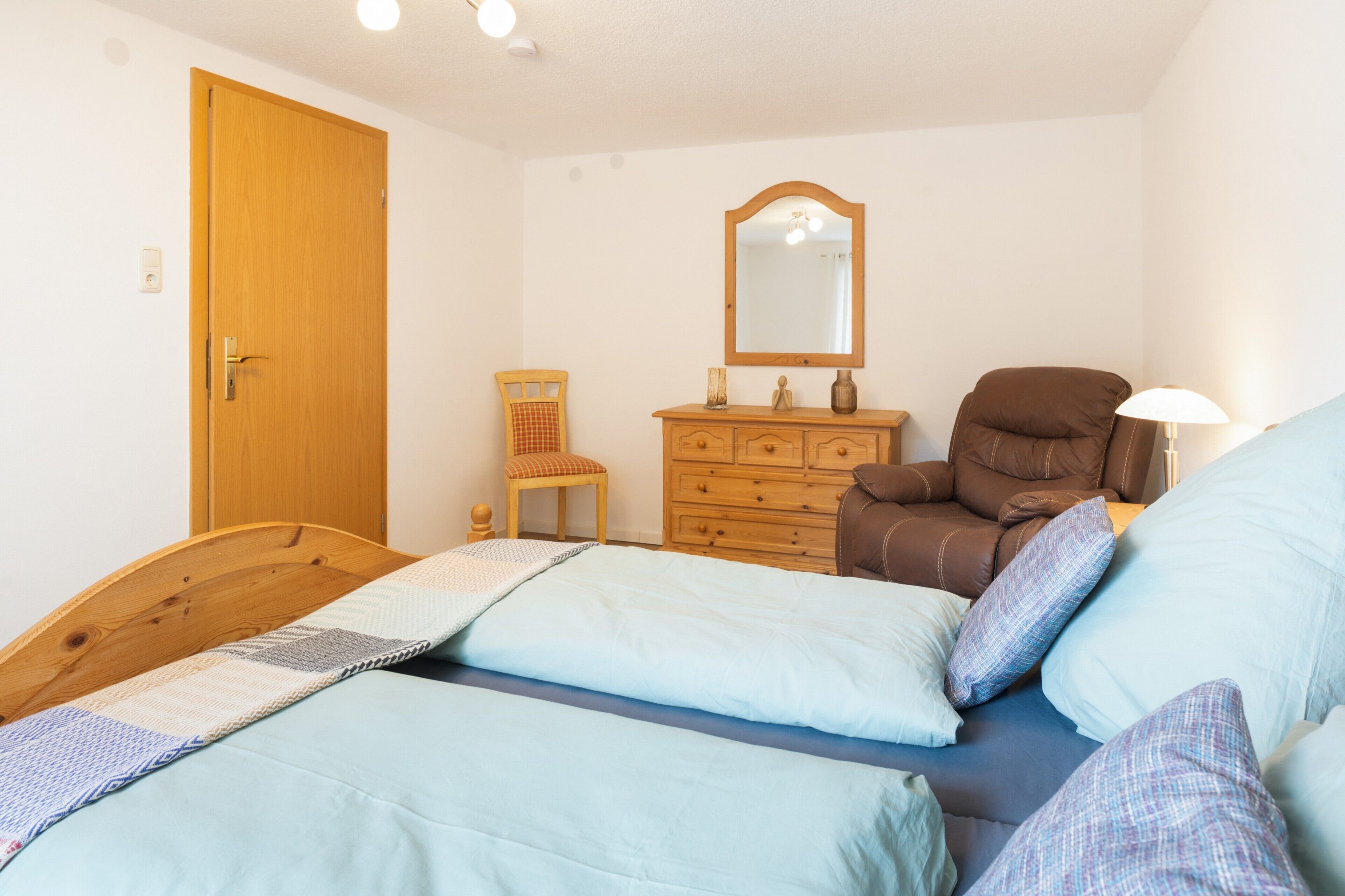 A bedroom with two beds, a wooden dresser, a chair, a mirror, and a lamp.