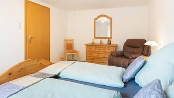 A bedroom with two beds, a wooden dresser, a chair, a mirror, and a lamp.