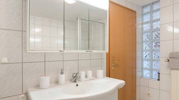 Une salle de bain avec un lavabo, un miroir et des toilettes, le tout de couleur blanche.