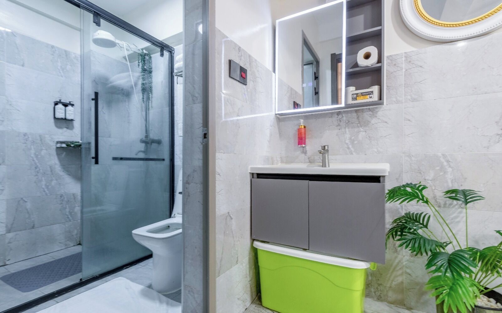 Ein modernes Badezimmer mit einer Duschkabine aus Glas, einer Toilette, einem Waschbecken mit Spiegel und einem grünen Mülleimer.