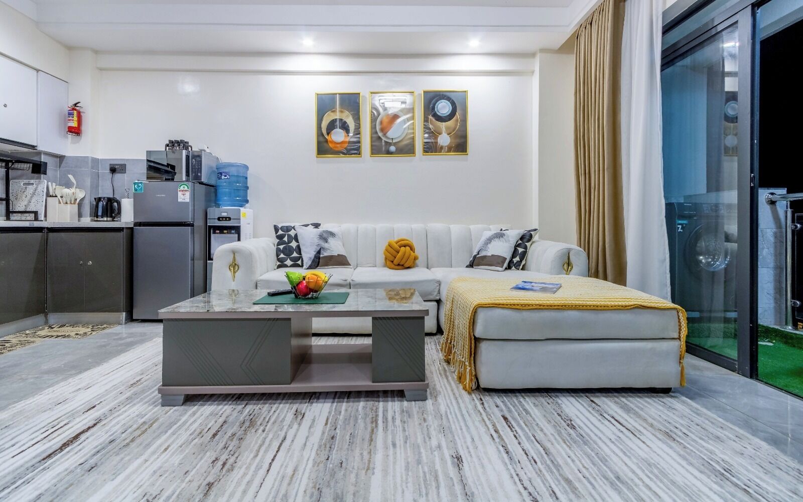 Una sala moderna con sofá, mesa de centro y un área de lavandería con paredes de vidrio.