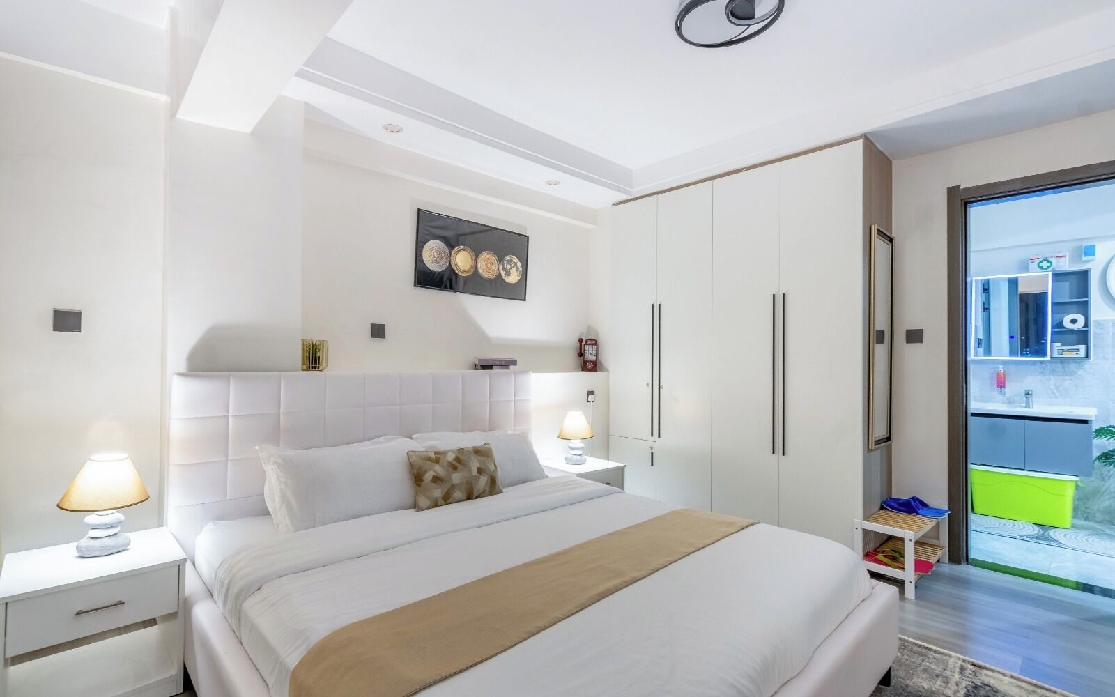 A modern bedroom with a bed, nightstands, a wall-mounted TV, and a sliding glass door to the balcony.