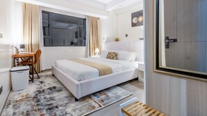 Habitación de hotel con cama, escritorio, silla y un pequeño cubo de basura.