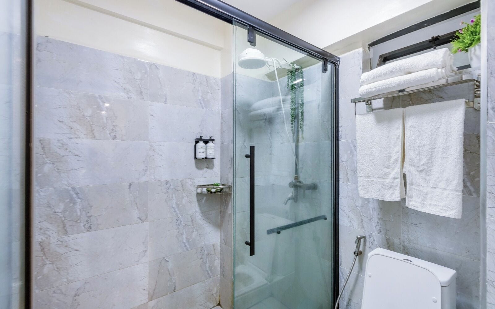 Une salle de bain moderne avec une douche à parois de verre, des carreaux de marbre et des serviettes soigneusement rangées.
