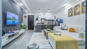 Una sala de estar moderna con televisor, sofá, mesa de centro y una cocina al fondo.