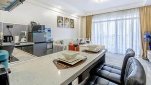 Una habitación de hotel moderna con cocina, comedor y un amplio ventanal con cortinas.