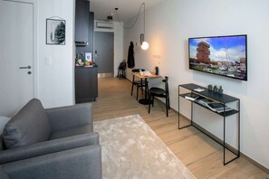 Un saló modern amb un sofà gris, una taula petita amb una làmpada, un televisor fixat a la paret i vista a un port esportiu.